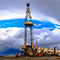 Una foto de una plataforma petrolera rodeada de trabajadores de servicios públicos y vehículos con un cielo azul nublado de fondo.